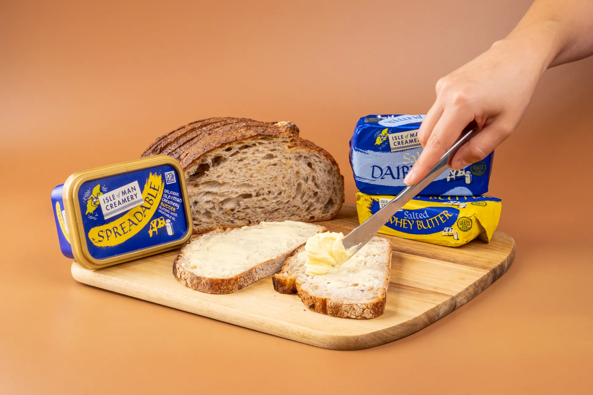 Product photography shot by DotPerformance for the Isle of Man Creamery Doorstep Delivery campaign, showing Isle of Man Creamery Spreadable butter and Salted Dairy Butter with sliced sourdough bread on a wooden board